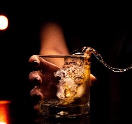 Kobieca ręka z impetem stawia szklankę z alkoholem na stół, płyn się rozlewa.